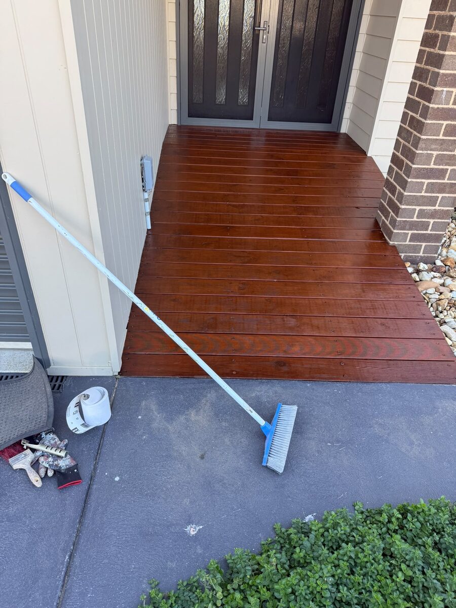 Deck being stained with a lambswool applicator on a pole